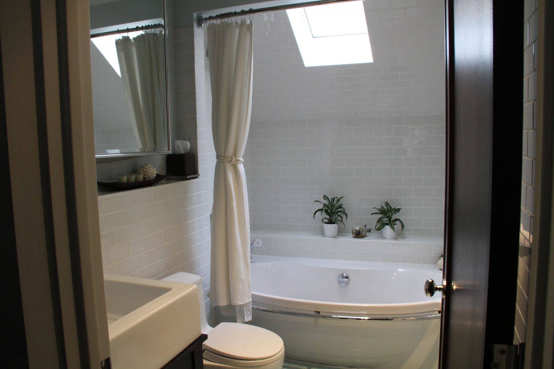 Small bathroom with a bathtub, toilet, sink, and skylight, shown in neutral tones