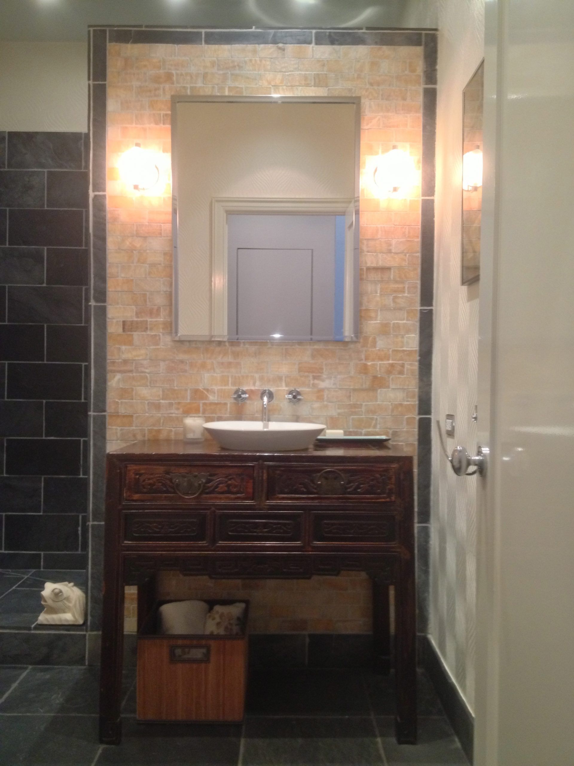 Bathroom vanity with mirror, sink, and wall sconces above dark tile flooring.