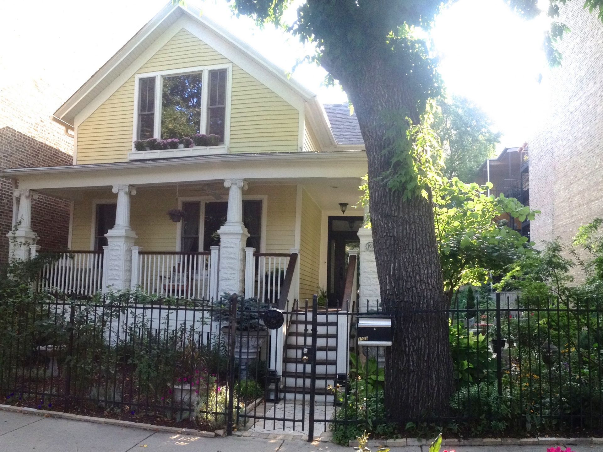 Yellow two-story house with white porch, black fence, and large tree in front