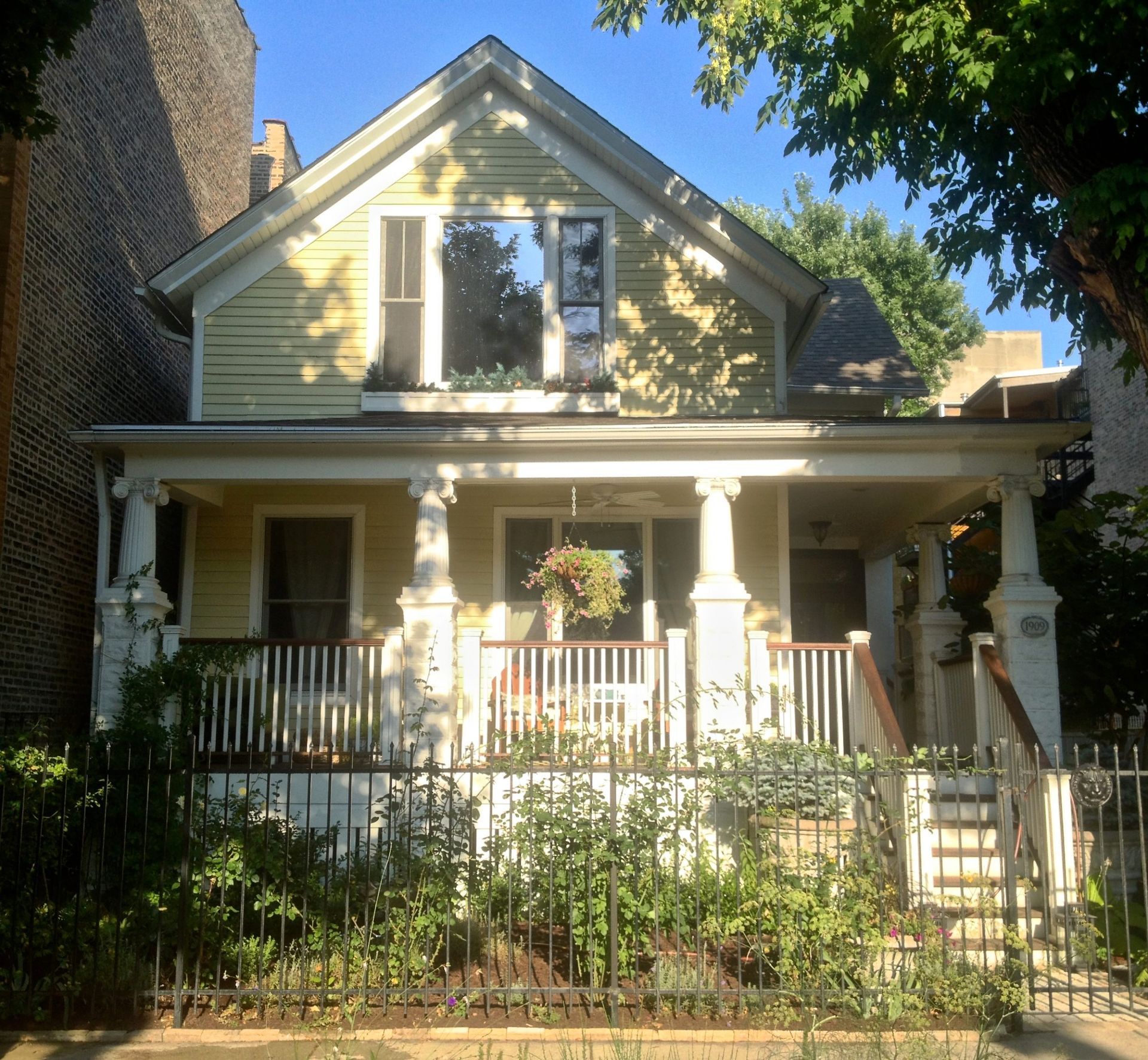Yellow two-story house with front porch, white trim, and iron fence in a leafy yard