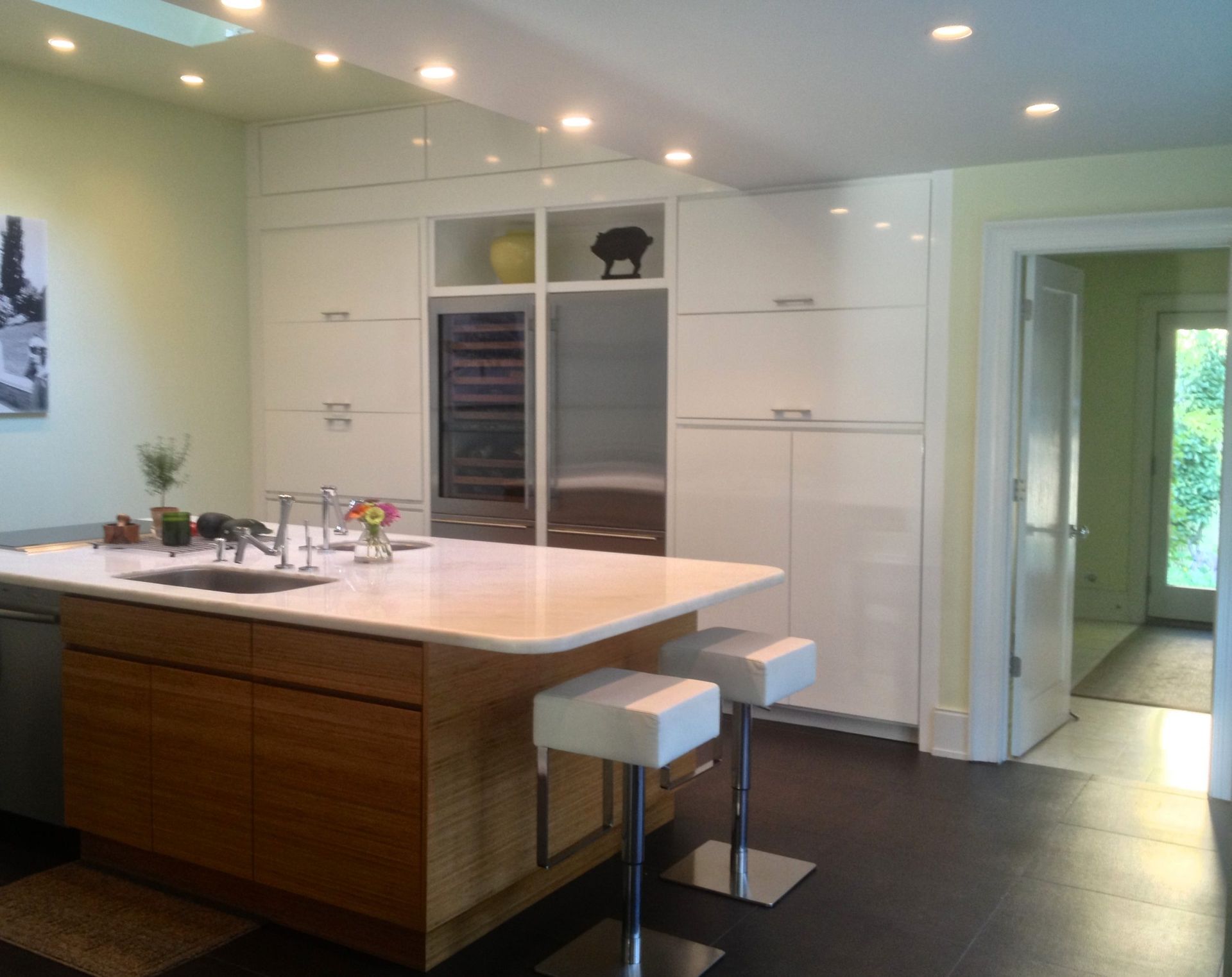 Modern kitchen with white cabinetry, wood island, and two stools under recessed lighting.
