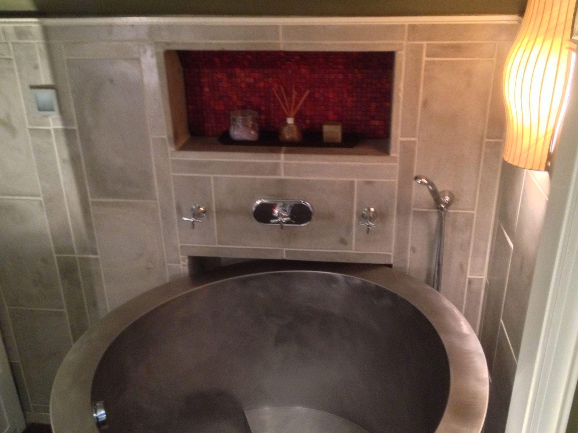 Modern bathroom with a large round sink, tiled walls, red mosaic niche, and wall sconce lighting