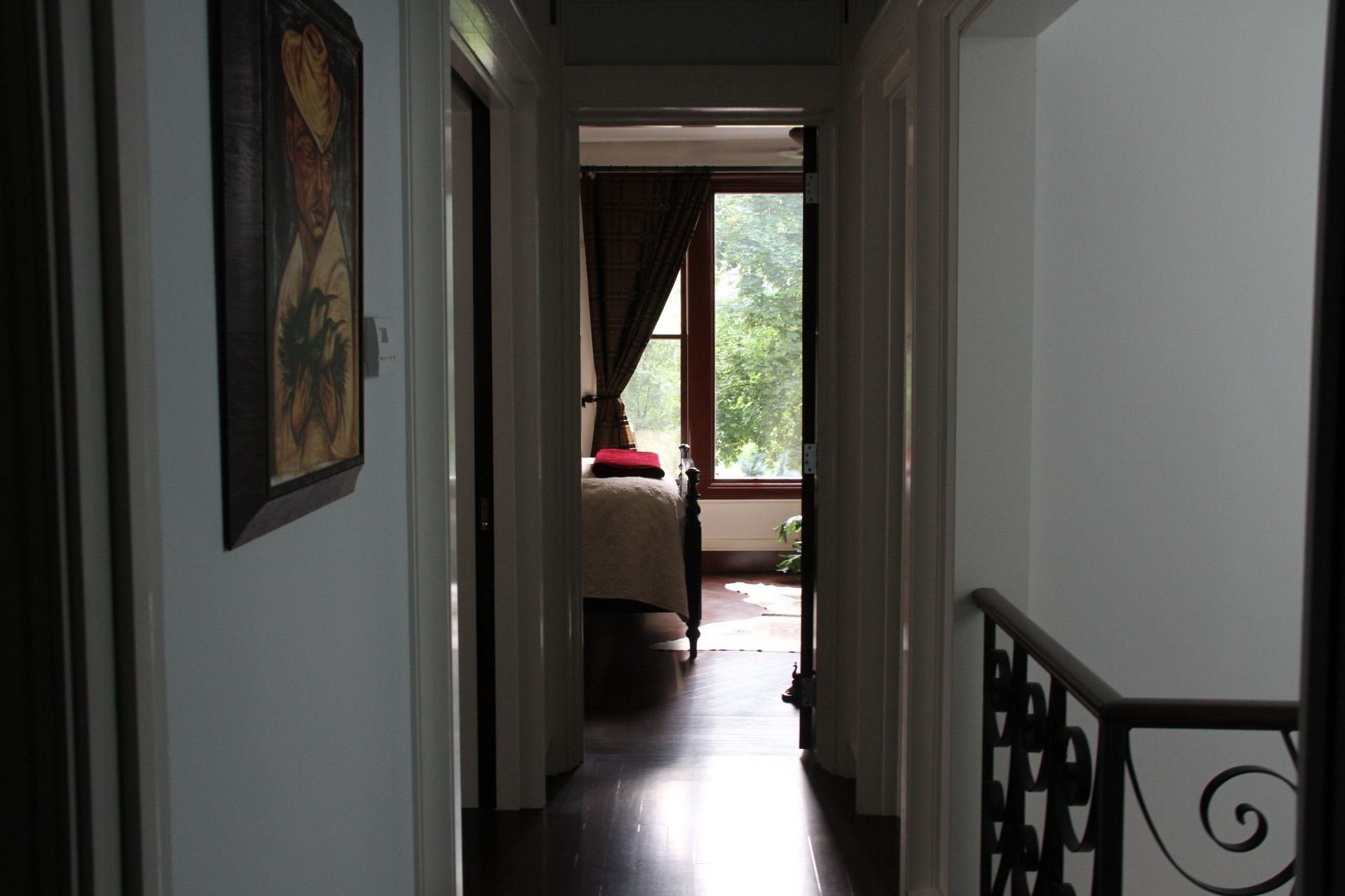 Narrow hallway with framed wall art, leading to a bright room with a window and red chair.