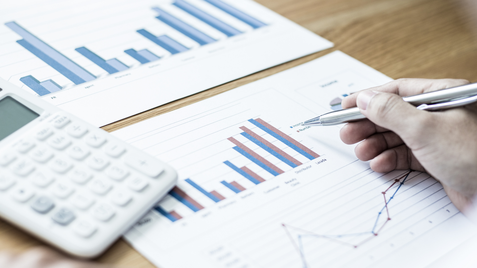 Hand with pen analyzing bar charts and calculator on a desk