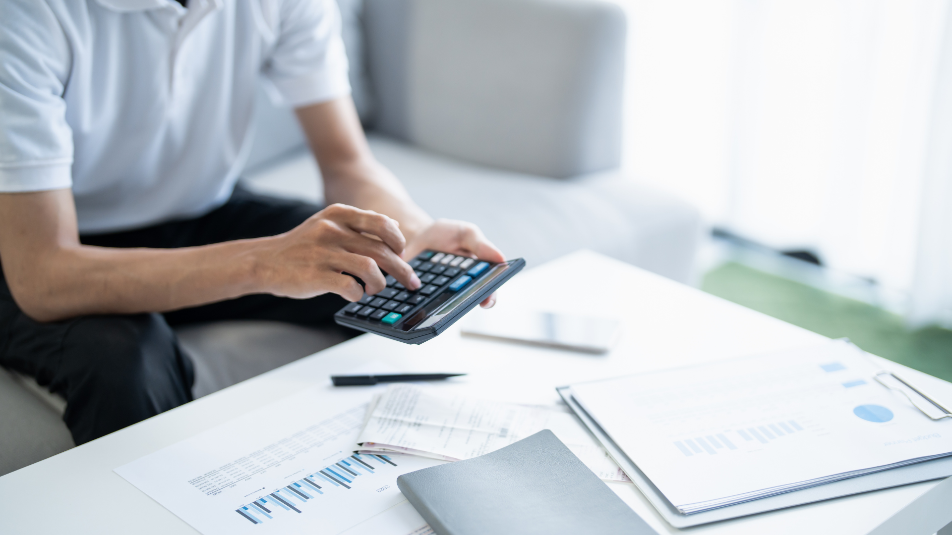 Person using a calculator at a desk with charts, papers, and a pen nearby