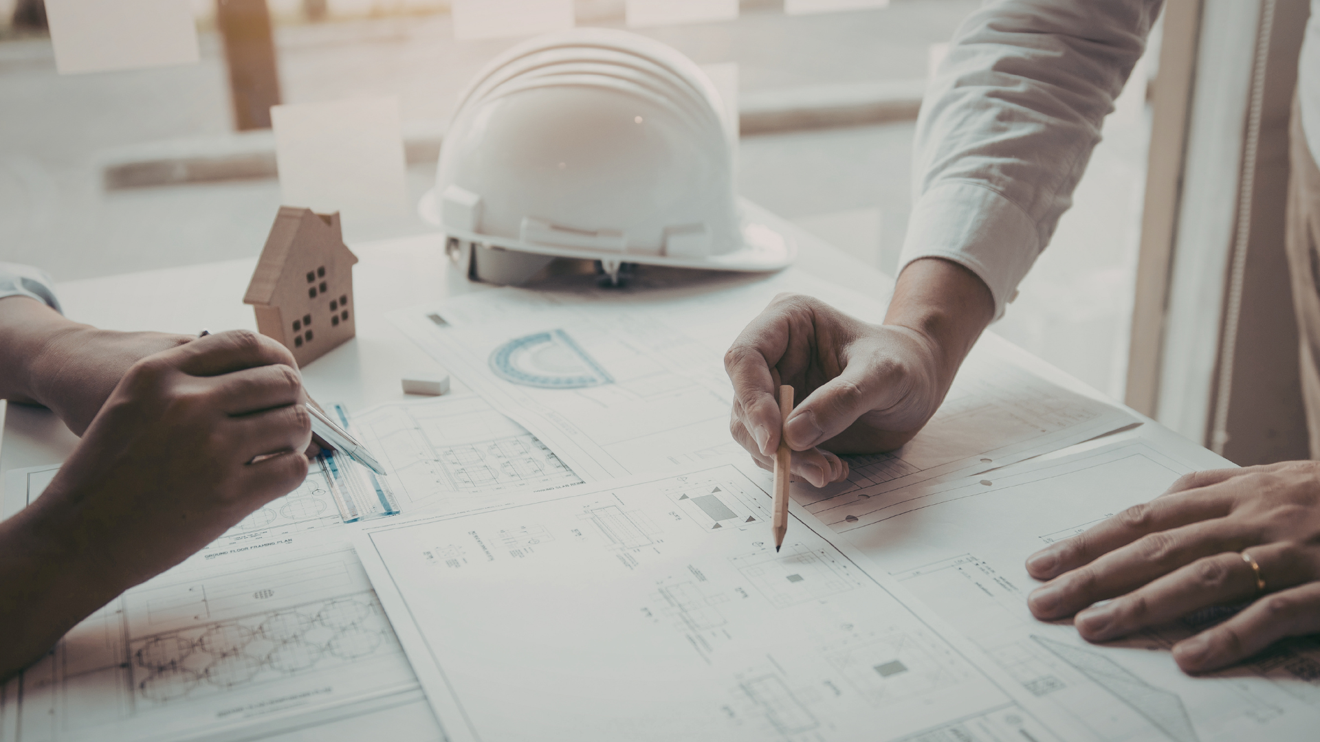 People reviewing building plans at a table with a hard hat and small house model