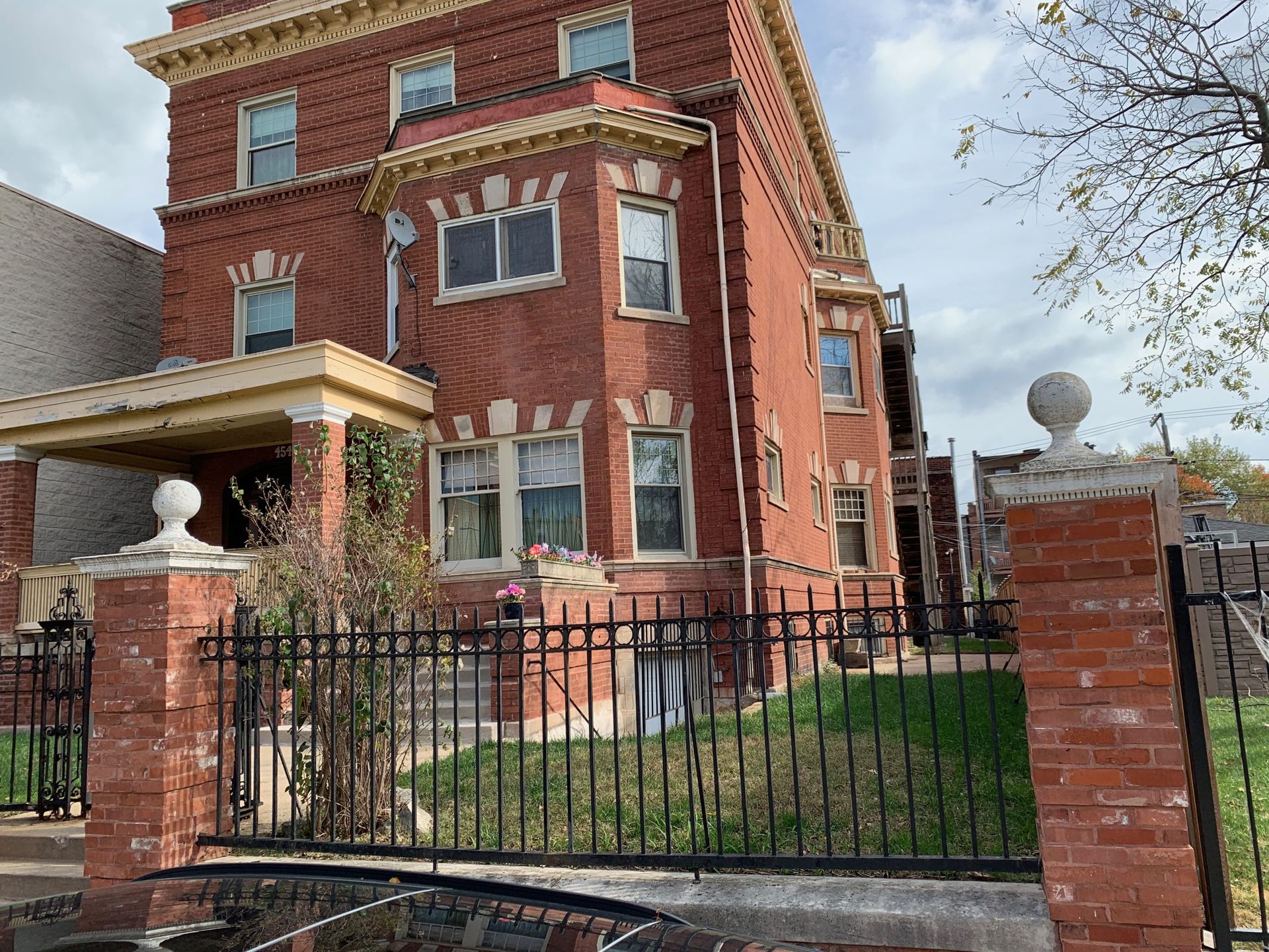 Red-brick historic house with iron fence and brick gate pillars under a cloudy sky