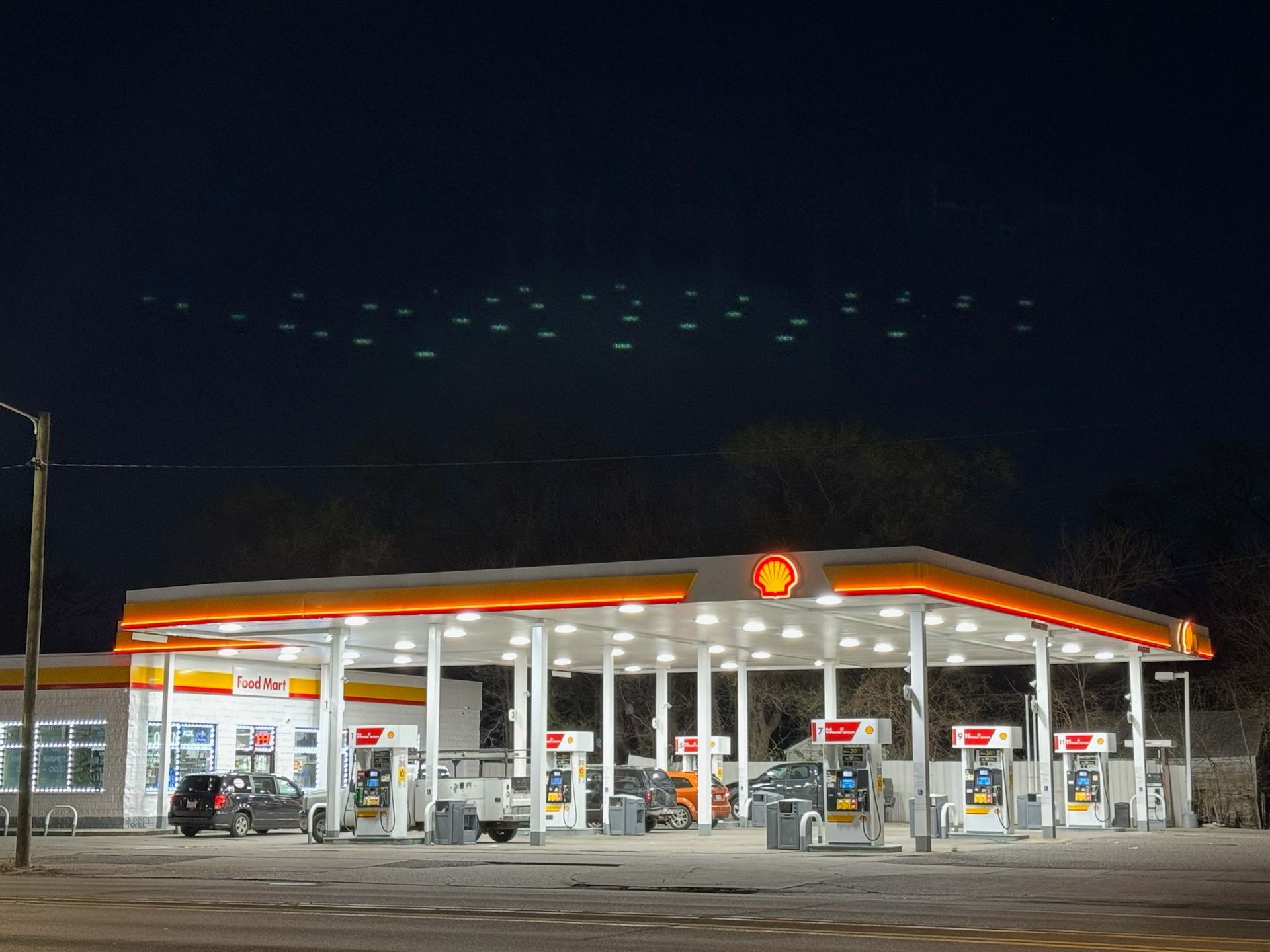 A gas station is lit up at night with cars parked in front of it.