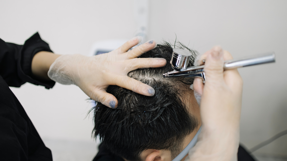 A woman is spraying a man 's hair with an airbrush.