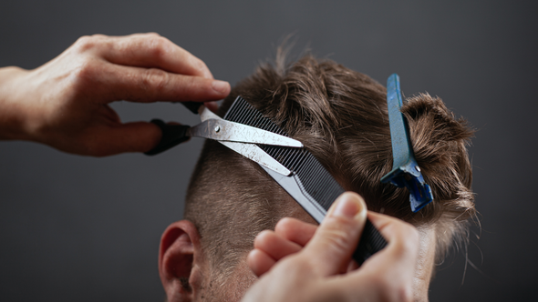 A man is getting his hair cut by a barber with scissors.