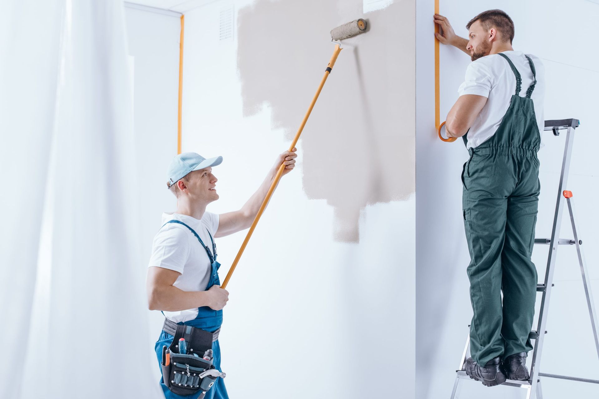 Two painters, one on a ladder, apply white paint to a wall.