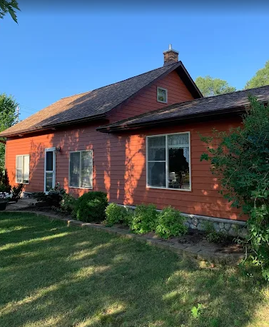House under construction, wood frame, unfinished roof, blue sky, dirt pile in front.
