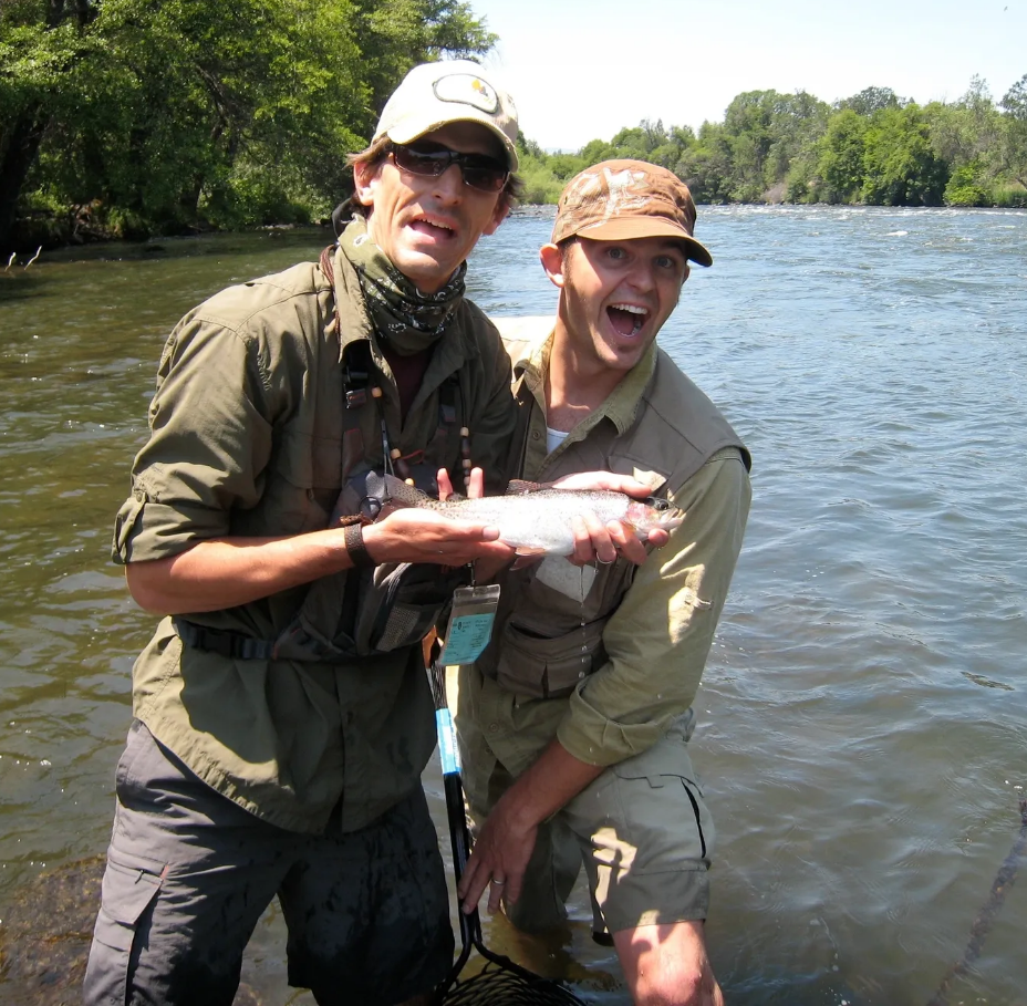 Two men holding a fish in front of a river