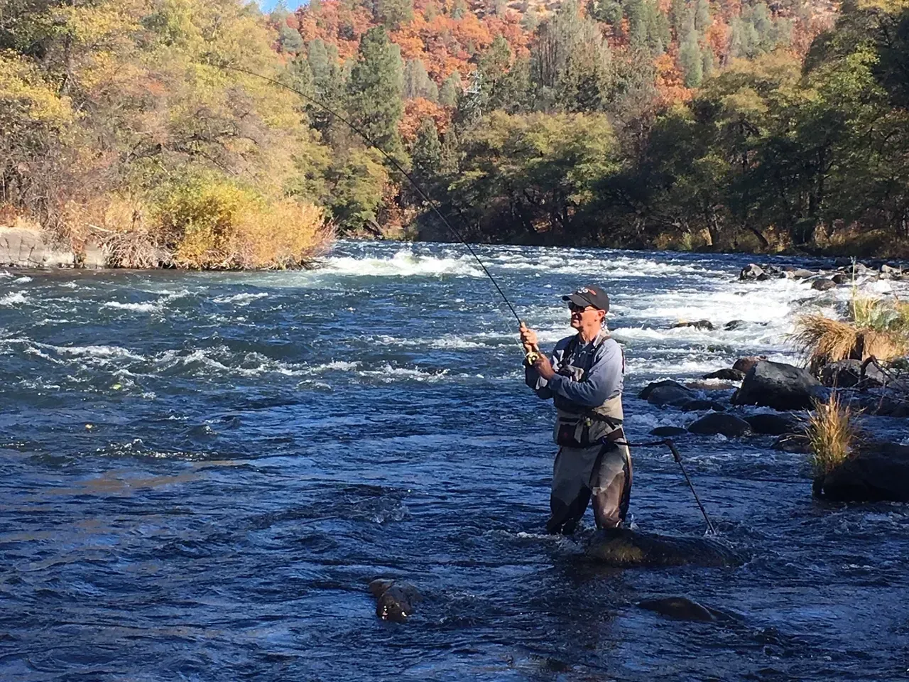 A man is fishing in a river with a fishing rod.