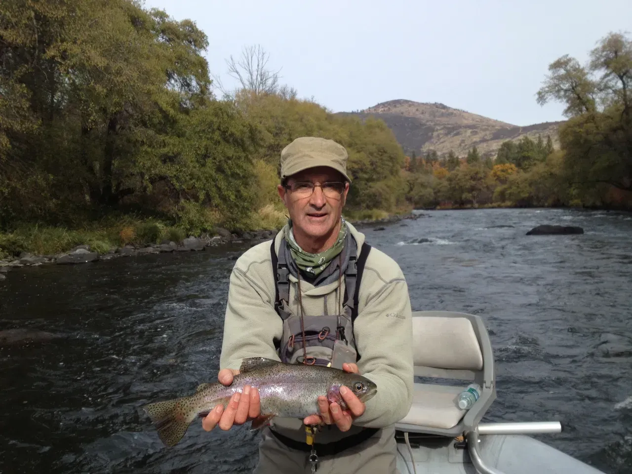 A man is holding a fish in front of a river.
