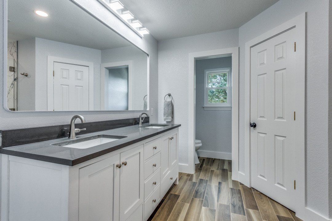 Bathroom with white cabinets, dark countertop, large mirror, and wood-look flooring.