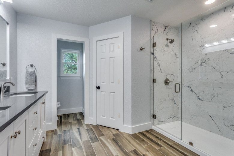 Bathroom with marble shower, white vanity, wood-look floor, and white door.