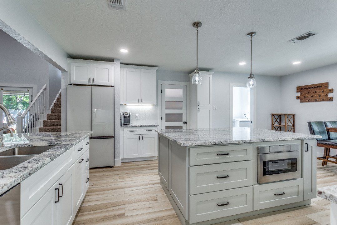 Modern white kitchen with island, marble countertops, stainless steel appliances, and wood flooring.