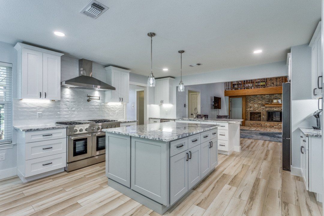 Modern kitchen with white cabinets, gray island, stainless steel appliances, and wood flooring.