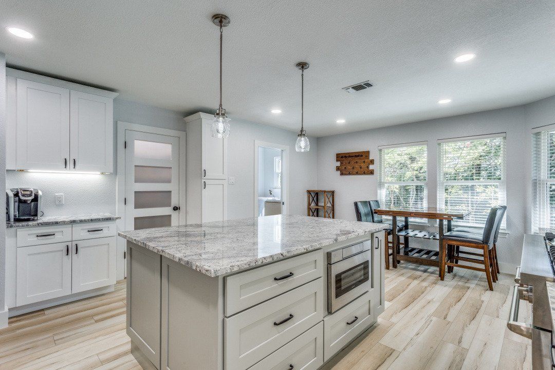 White kitchen with island, cabinets, granite countertops, and light wood flooring.