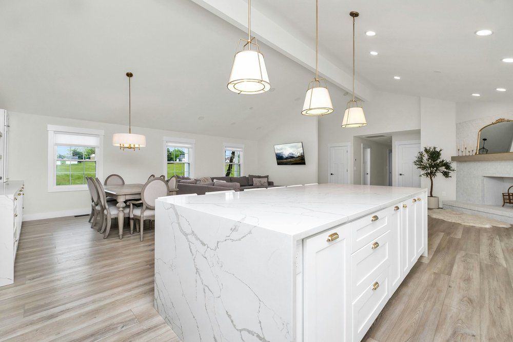 Modern white kitchen with island and dining area, light wood floors, and pendant lighting.