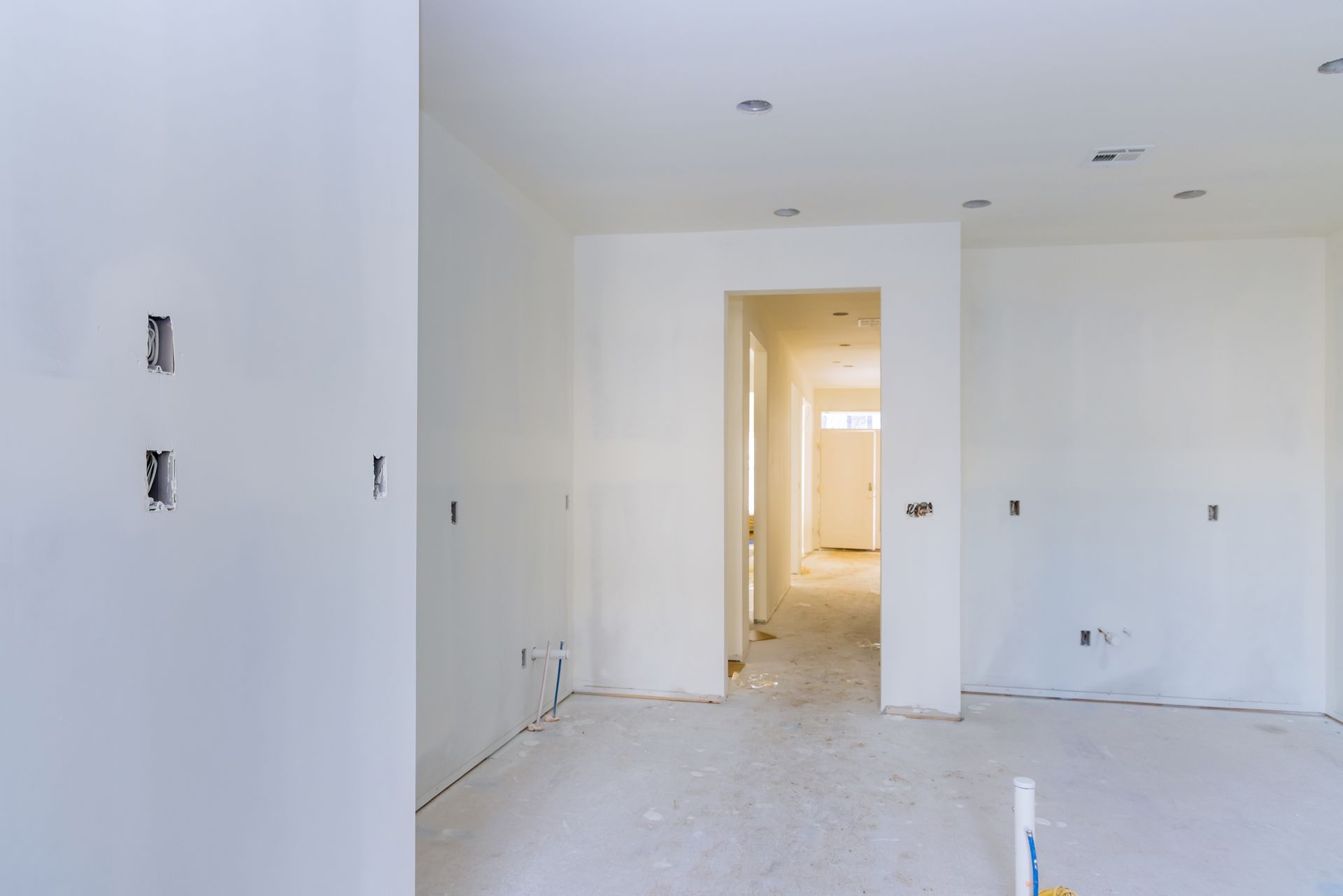 Interior of a room under construction, with white walls, exposed electrical outlets, and a doorway leading to a hallway.
