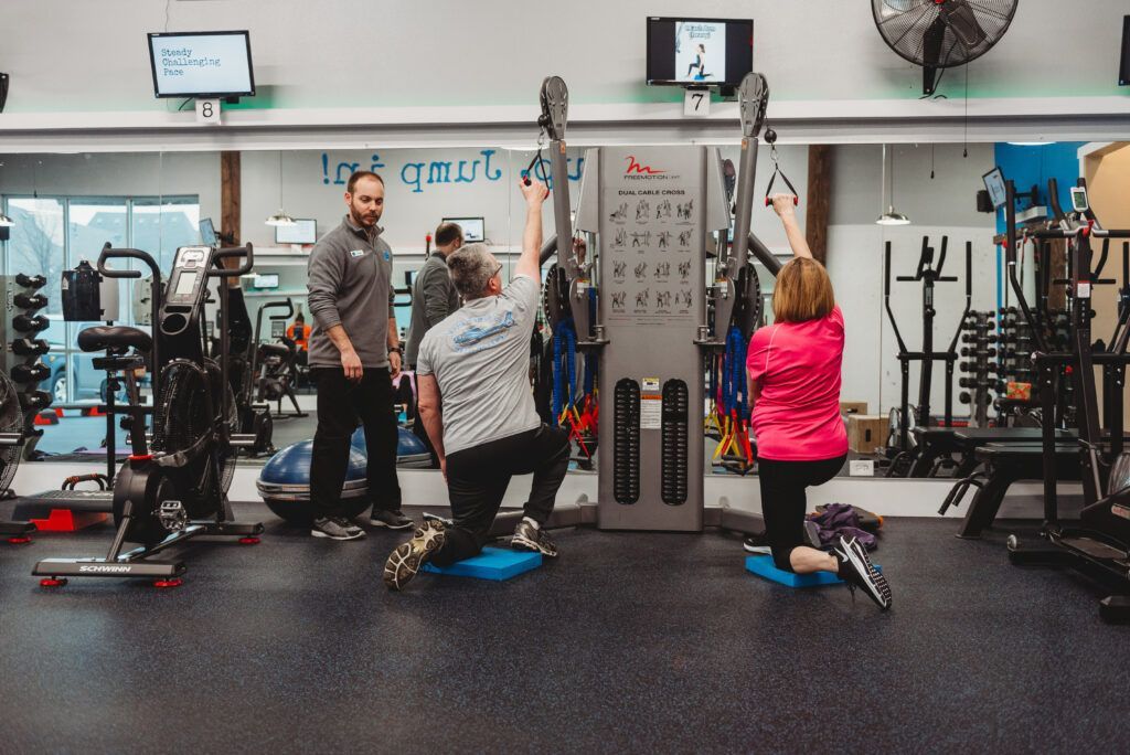 People working out with a trainer at a gym using a cable machine.