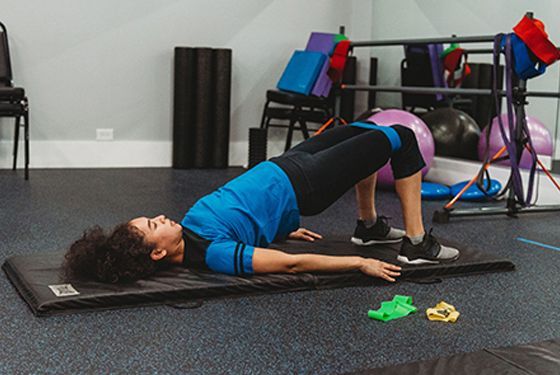 Person doing a bridge exercise with a resistance band in a gym.