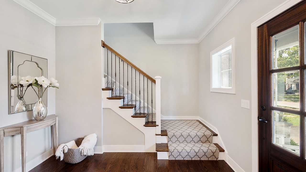 A hallway featuring a staircase leading up and a white window at the end.