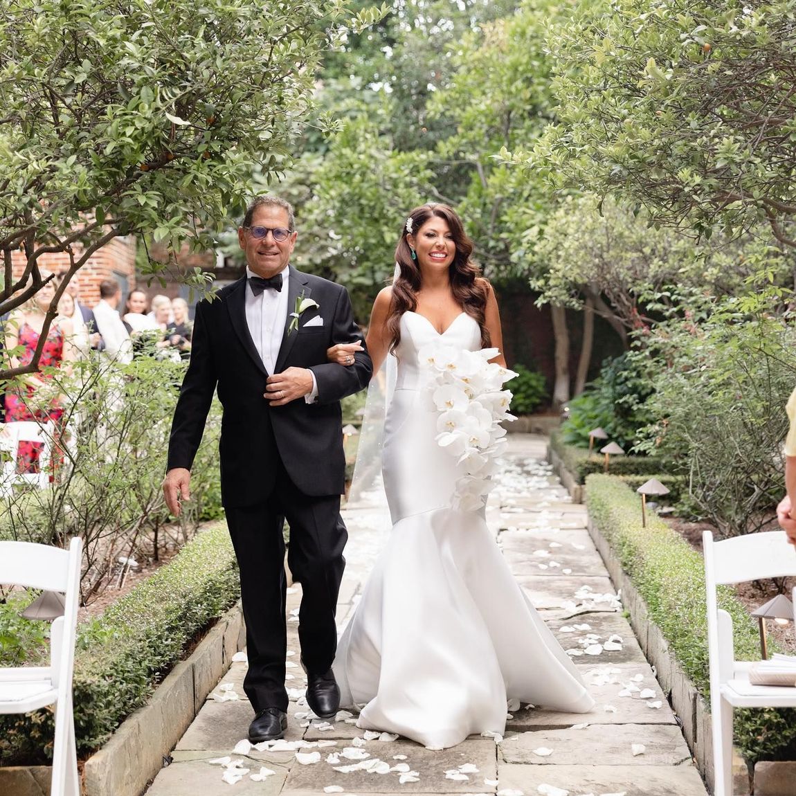 Bride in white gown walks down aisle with man in suit at outdoor wedding.