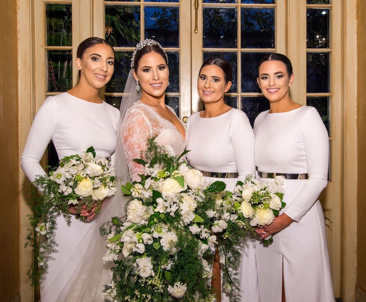 A bride and her bridesmaids are posing for a picture in front of a window.
