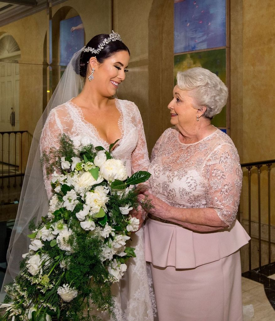 A bride and her mother are standing next to each other holding a bouquet of flowers.