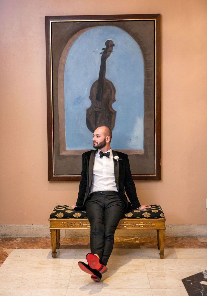 A man in a tuxedo is sitting on a bench in front of a painting of a violin.