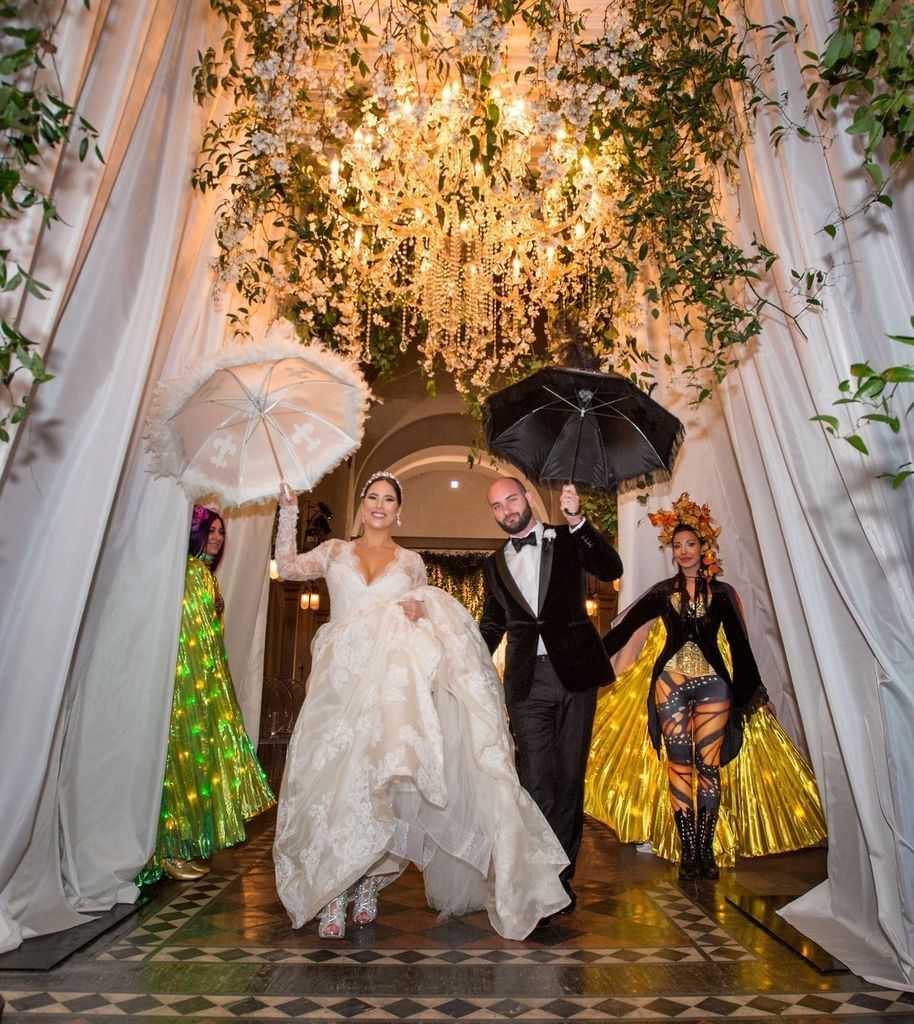 A bride and groom are walking through a tunnel holding umbrellas.