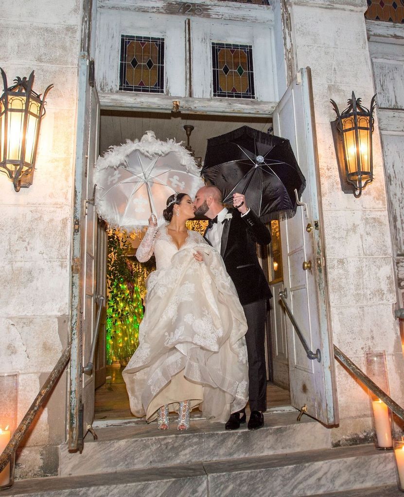 A bride and groom are kissing in the doorway of a building while holding umbrellas.