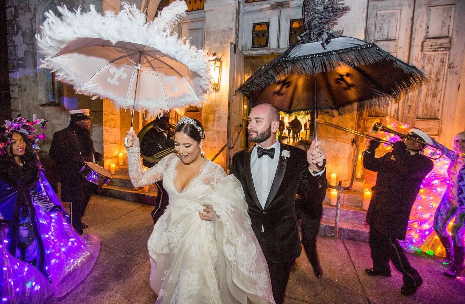 A bride and groom are walking down the street with umbrellas.