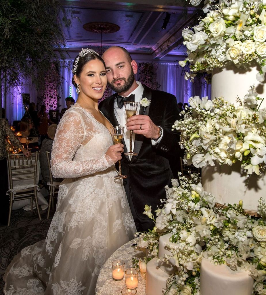 A bride and groom are posing for a picture in front of a wedding cake.