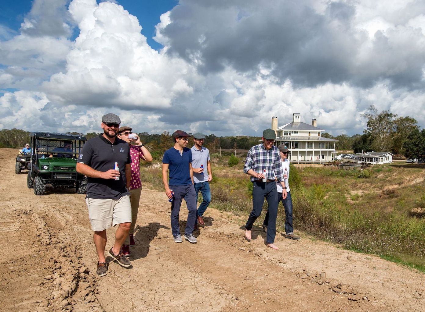 A group of people are walking down a dirt road in front of a house.