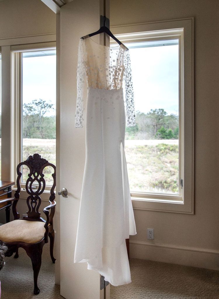 A wedding dress is hanging on a door next to a window.