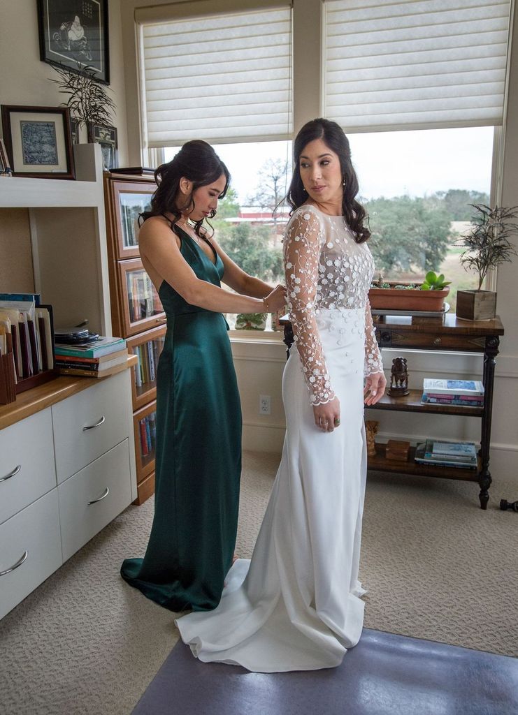 A woman in a green dress is helping a woman in a white dress get ready for her wedding.