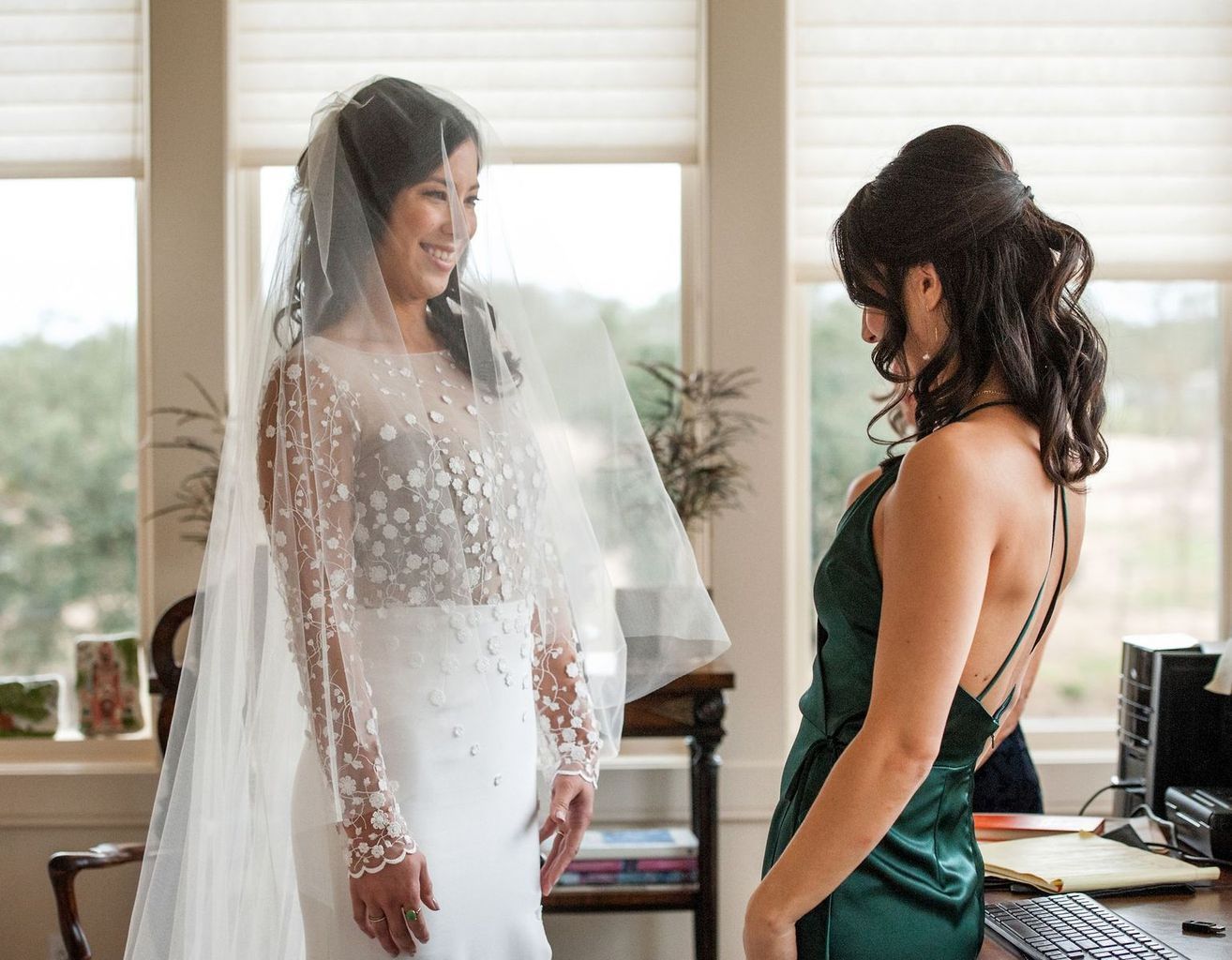 A bride and her bridesmaid are standing next to each other in a room.
