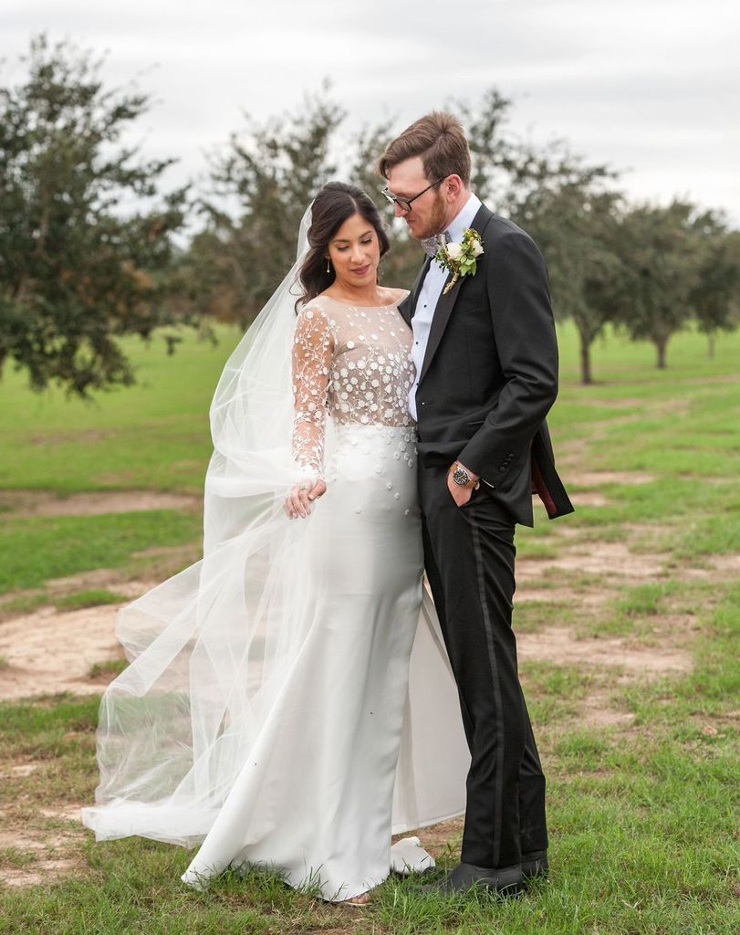 A bride and groom are posing for a picture in a field.