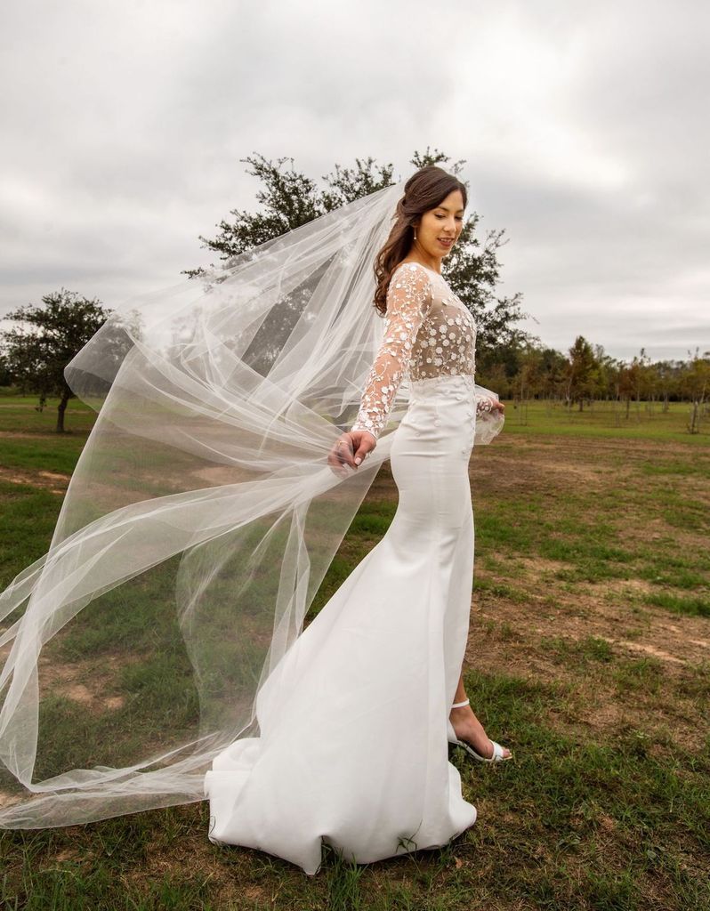 A woman in a wedding dress and veil is standing in a field.
