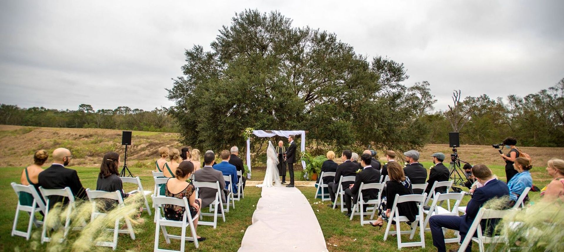 A group of people are sitting in chairs at a wedding ceremony in a field.
