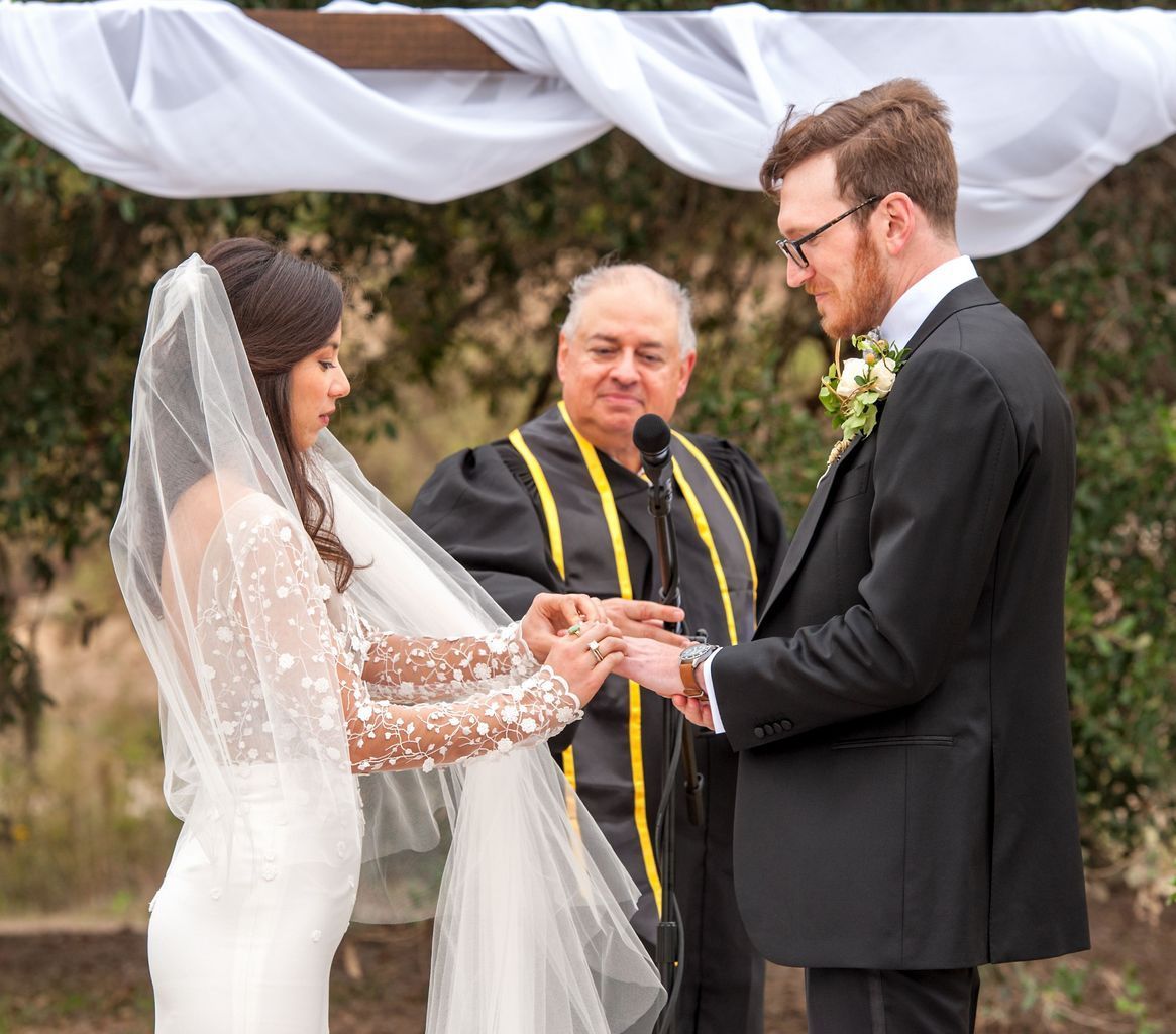 A bride and groom are getting married and the groom is putting the ring on the bride 's finger.