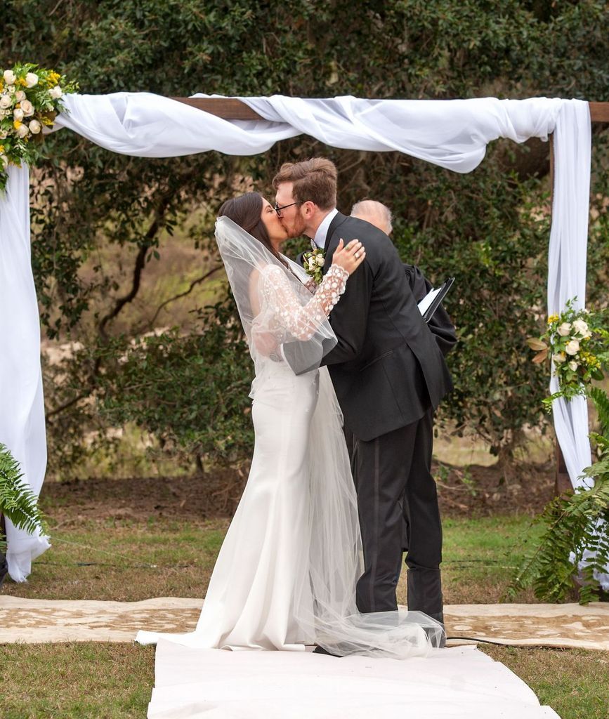 A bride and groom kissing at their wedding under a white arch