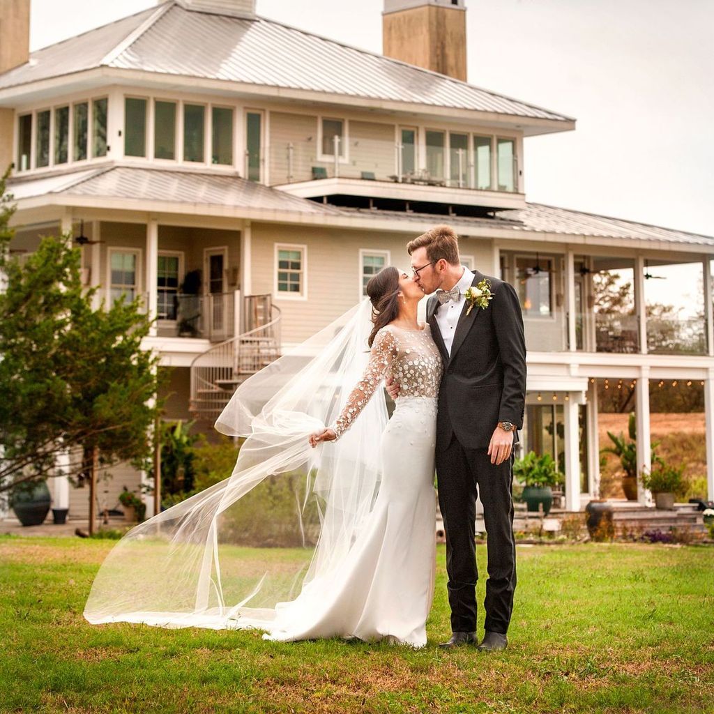 A bride and groom kissing in front of a large house