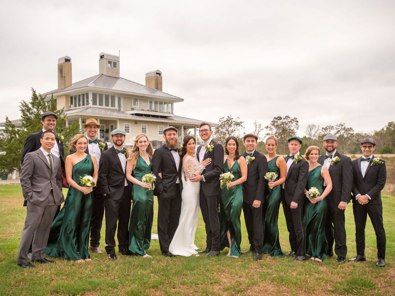 The bride and groom are posing for a picture with their wedding party in front of a large house.