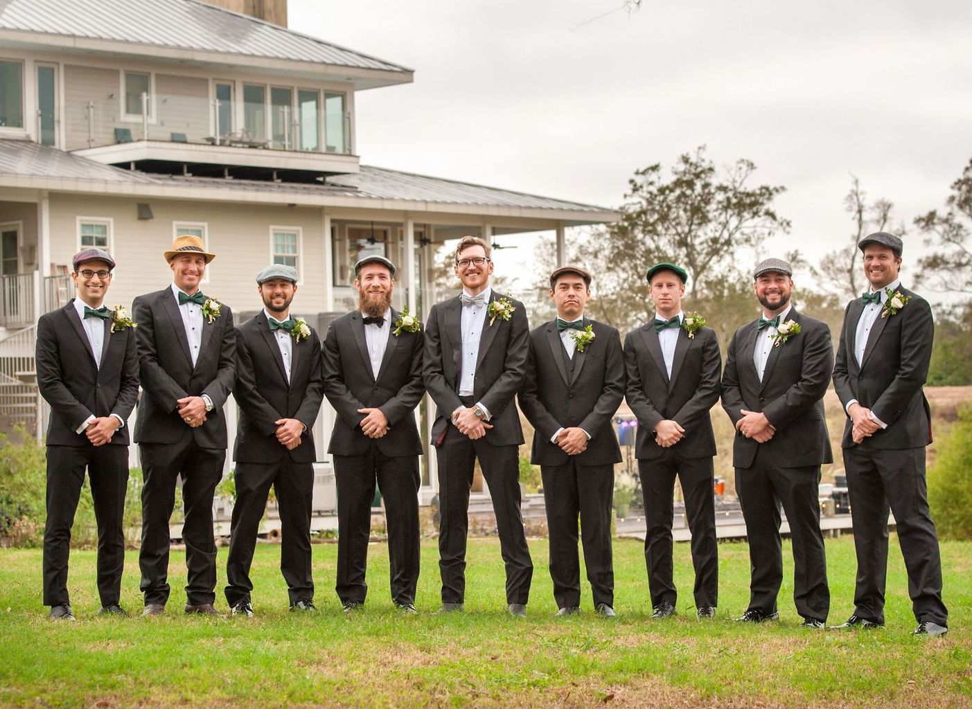 The groom and his groomsmen are posing for a picture in front of a large house.