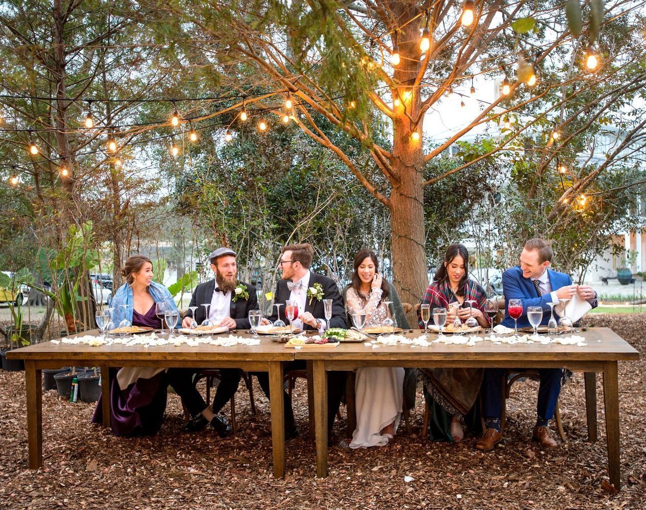 A group of people are sitting at a long table under a tree.
